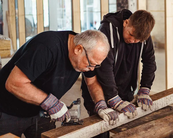 Menschen bearbeiten in einer Werkstadt ein Holzbrett im Stehen