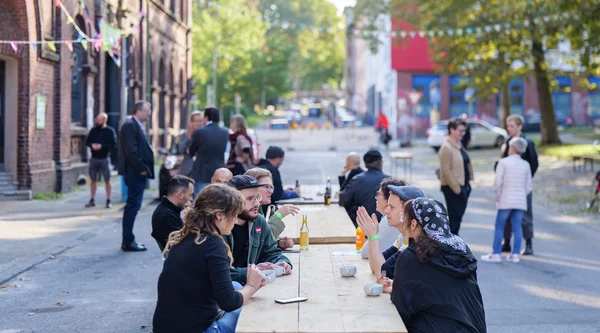 Menschen sitzen an Holzbänken vor der Quartiershalle der KoFabrik in Bochum.
