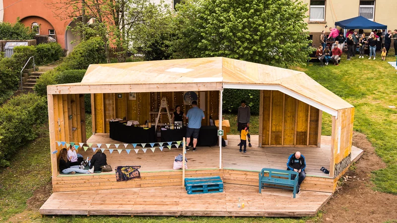 Eine Holzüberdachung auf einer Wiese mit Menschen