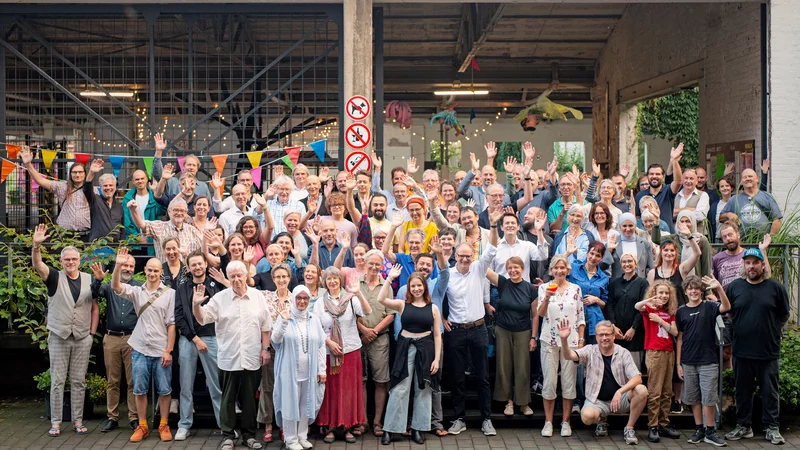 Etwa Hundert Personen stehen vor der Shedhalle der Samtweberei in Krefeld und winken in die Kamera