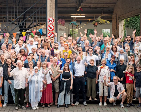 Etwa Hundert Personen stehen vor der Shedhalle der Samtweberei in Krefeld und winken in die Kamera