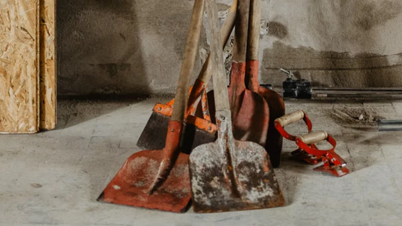 An einer frisch verputzten Wand lehnen mehrere Schaufeln und Kehrbesen