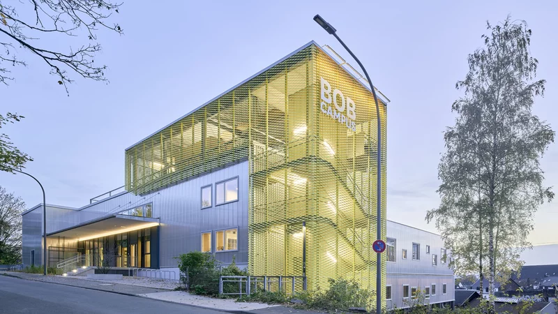 Der gelbe Aufzugturm vom BOB CAMPUS in Wuppertal-Oberbarmen und das Fabrikgebäude sind stark erleuchtet zu sehen.