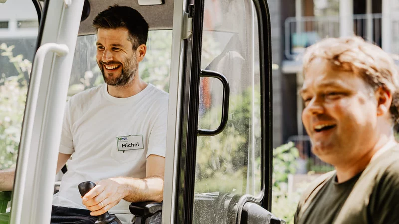 Mensch sitzt in Gartentraktor, fröhlicher Mensch steht daneben