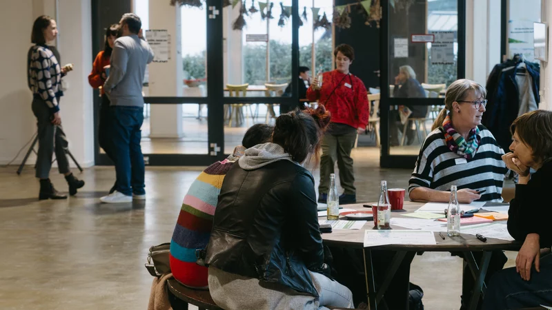 Eine Gruppe Menschen sitzt in der Nachbarschaftsetage des BOB CAMPUS um einen Tisch. Im Hintergrund führt eine Glaswand zur Viertelsküche.