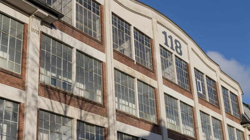Außenansicht der Wiesenwerke, Wiesenstraße 118 in Wuppertal. Zu sehen ist eine Gebäudefassade mit großen FEnsterflächen und der Hausnummer 118 im Giebel vor blauem Himmel.