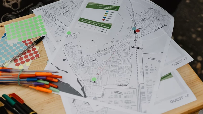 Auf einem Tisch draußen liegen Stifte und Klebepunkte und eine Karte eines Stadtteils auf einem weißen Papier. Dort können Informationen eingetragen werden.