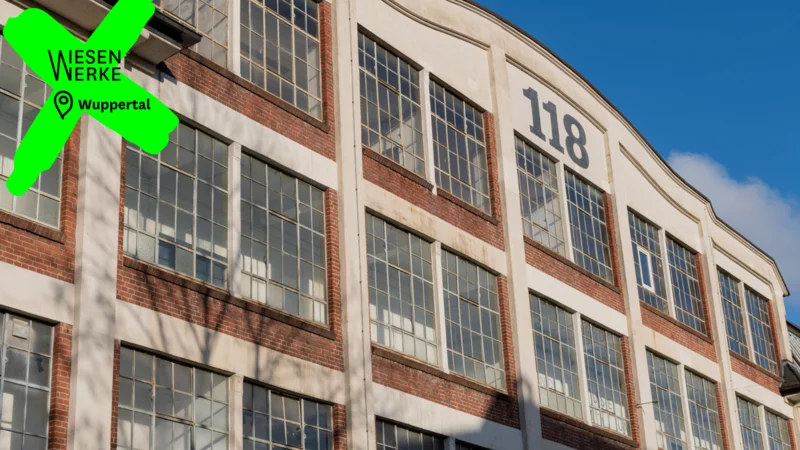 Außenaufnahme einer Textilfabrik mit großen Fenstern und der Hausnummer 118. Durch ein Logo und eine Ortsangabe ist das Bild deutlich als Wiesenwerke in Wuppertal gekennzeichnet.
