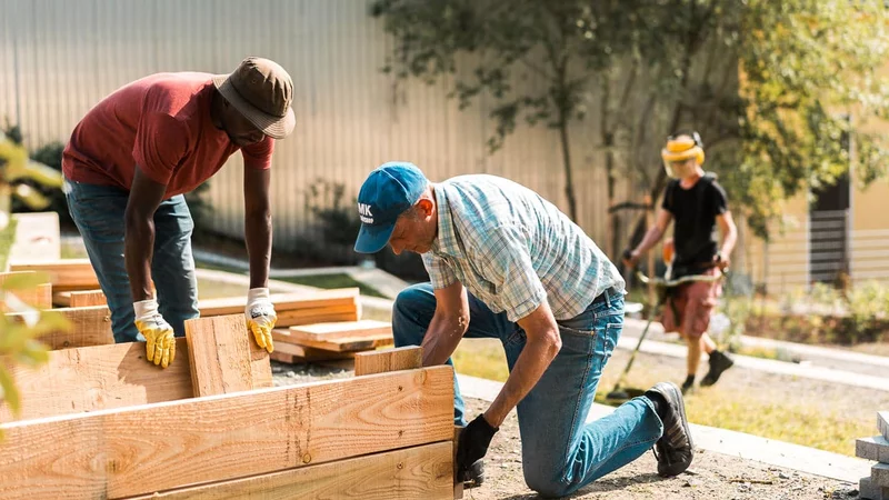 Menschen knien bei der Befestigung von Holzbrettern in einem Garten