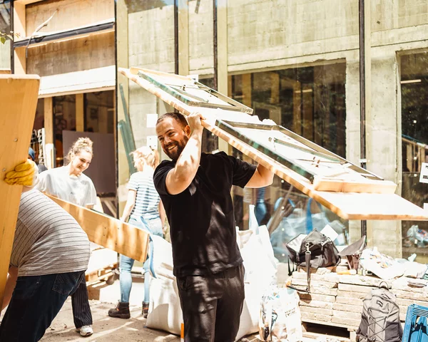 Fröhliche Menschen auf einer Baustelle tragen Gartentische/Bierbänke
