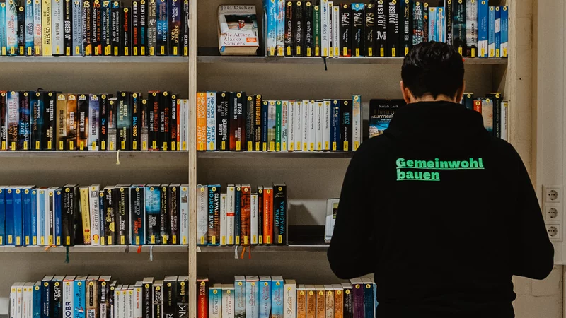 Mensch mit einem "Gemeinwohl Bauen"-Pulli vor einem Bücherregal